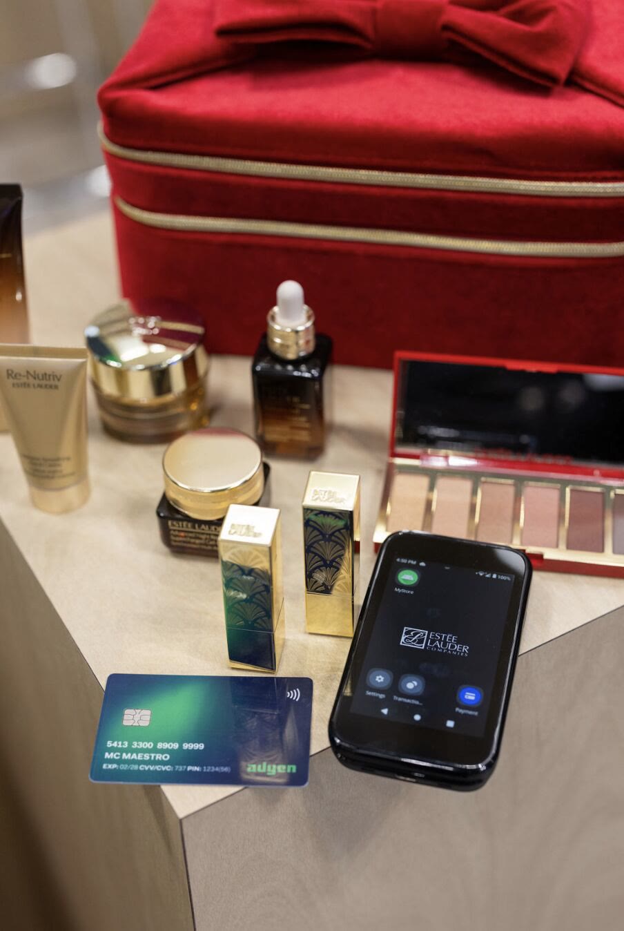 An Adyen Android payment device showing the Estée Lauder app on a beauty counter, next to an Adyen test card